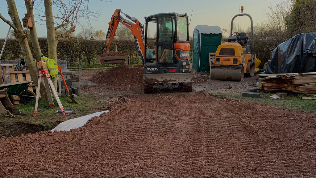 A CTC mini excavator and roller compacting a newly laid stone access track