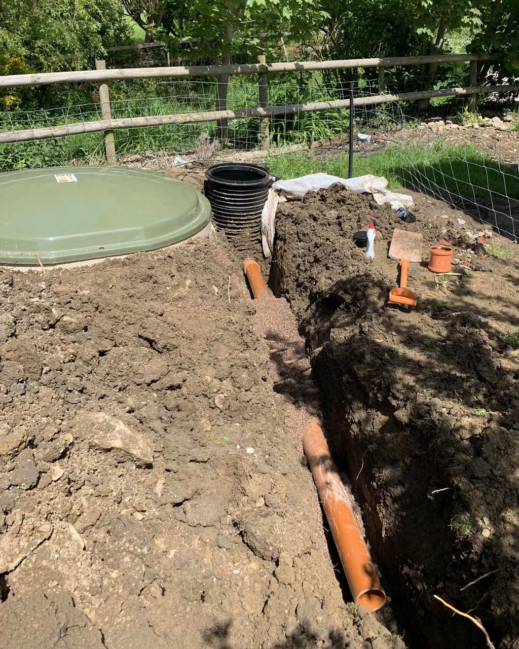 New orange drainage pipe laid in an open trench alongside a treatment tank and inspection chambers