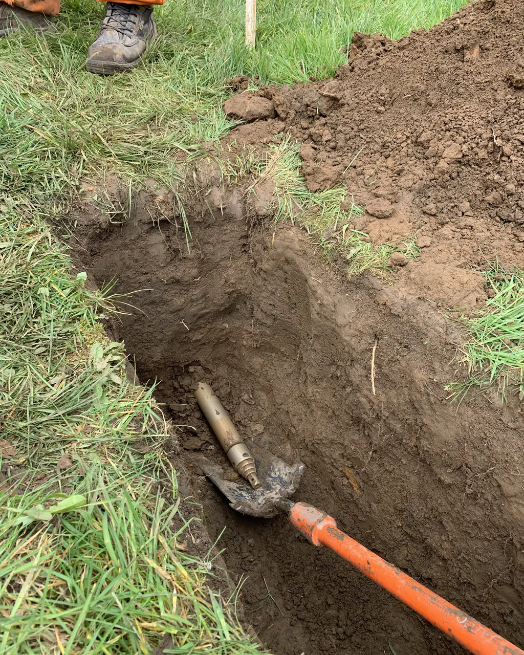 An excavated trench exposing an old water service connection joined to new orange service pipe