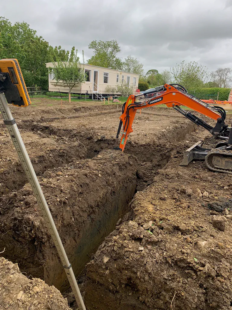 An excavator digging a deep service trench at a park homes site